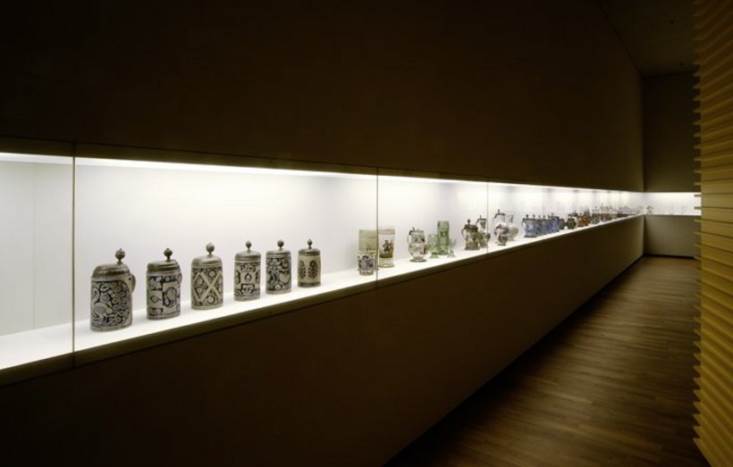 Ausstellungsansicht: abgedunkelter Raum, eine lang gezogene Vitrine mit Keramikgefässen
