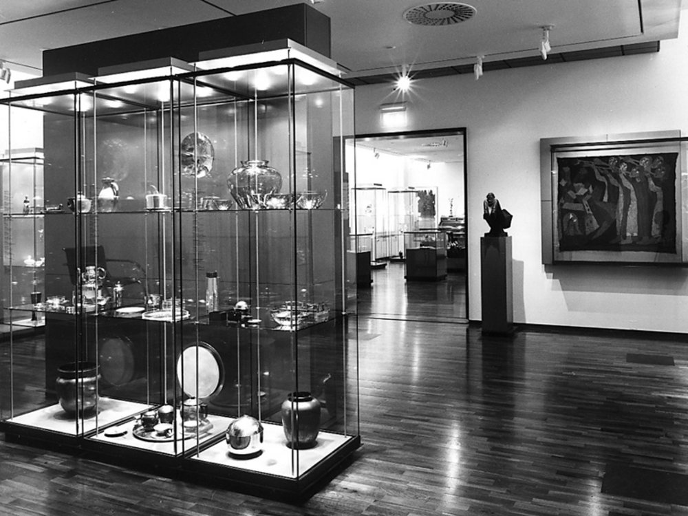 schwarz-weiß Fotografie einer Ausstellungsansicht, im Vorgerund eine große Vitrine mit Objekten