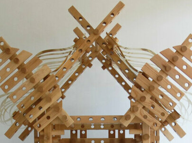 : Eine Skulptur aus Holzlatten, die zu einem komplexen, turmartigen Gebilde zusammengefügt sind