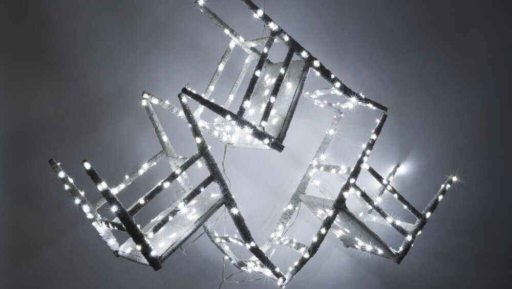 Ein Kunstwerk aus drei ineinander übergehenden Stühlen die mit mit weißen LEDs geschmückt sind.
