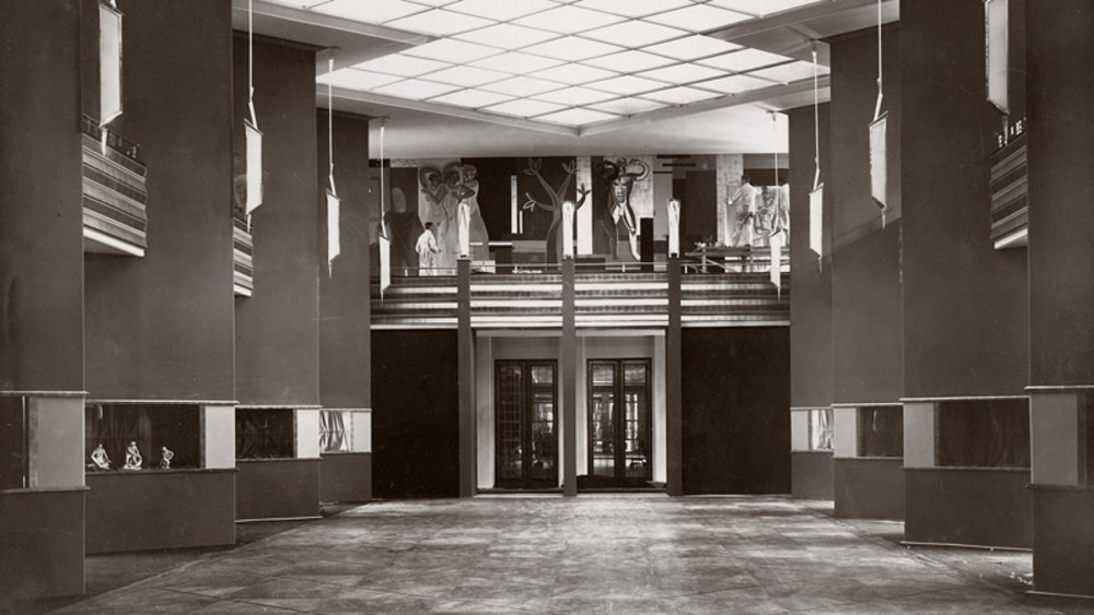 schwarz-weiß Fotografie der Pfeilerhalle, links und rechts die Pfeiler, in der Mitte leere Ausstellungsfläche und zwei große Zugangstüren