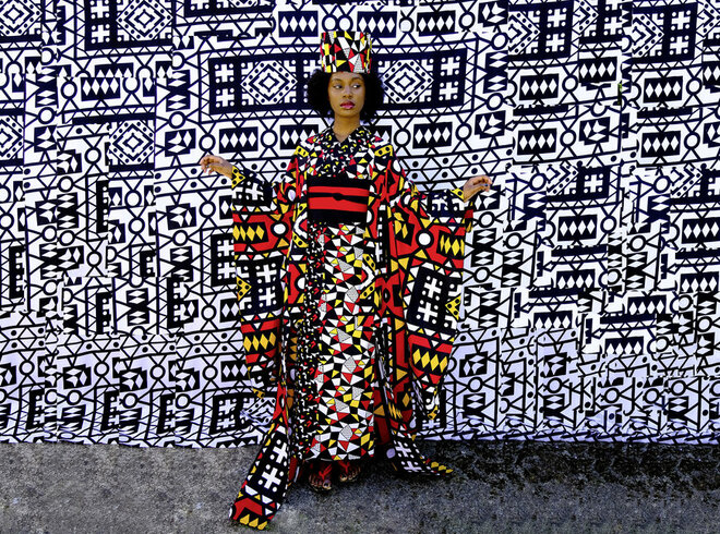 Modell in ethnisch inspiriertem Print-Kleid vor einer Wand mit schwarz-weißem grafischem Muster, das einen starken visuellen Kontrast erzeugt, perfekt für kulturell beeinflusste Mode und Street-Style-Fotografie