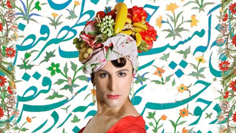 Eine Fotomontage zeigt eine Frau, die einen roten Schal und einen Kopfschmuck aus Früchten und Blumen trägt, auf einem Hintergrund mit floralem Muster. Ihr Körper geht nahtlos in das Bild eines Pfaus über, dessen prächtiges, farbenfrohes Federkleid hinter ihr auffächert