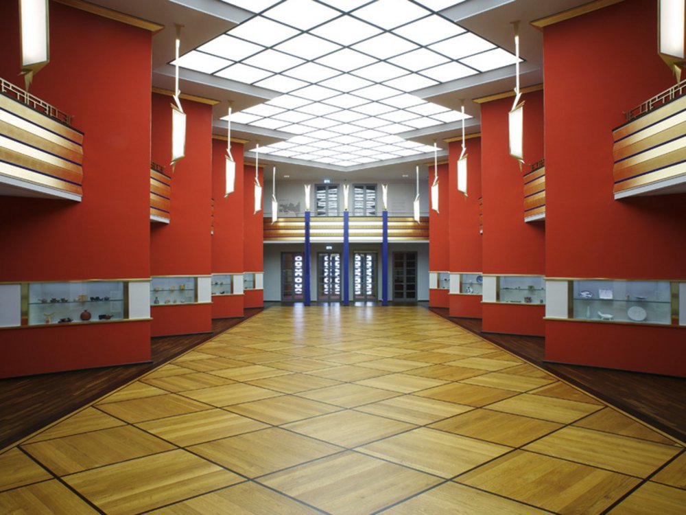 Fotografie der Pfeilerhalle, links und rechts die Pfeiler, in der Mitte leere Ausstellungsfläche und zwei große Zugangstüren