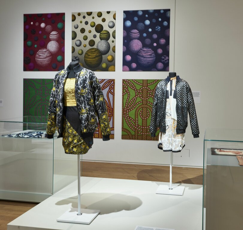 Innenansicht einer Kunstgalerie mit einer Vielfalt an ausgestellten Bildern und Kleidungsstilen