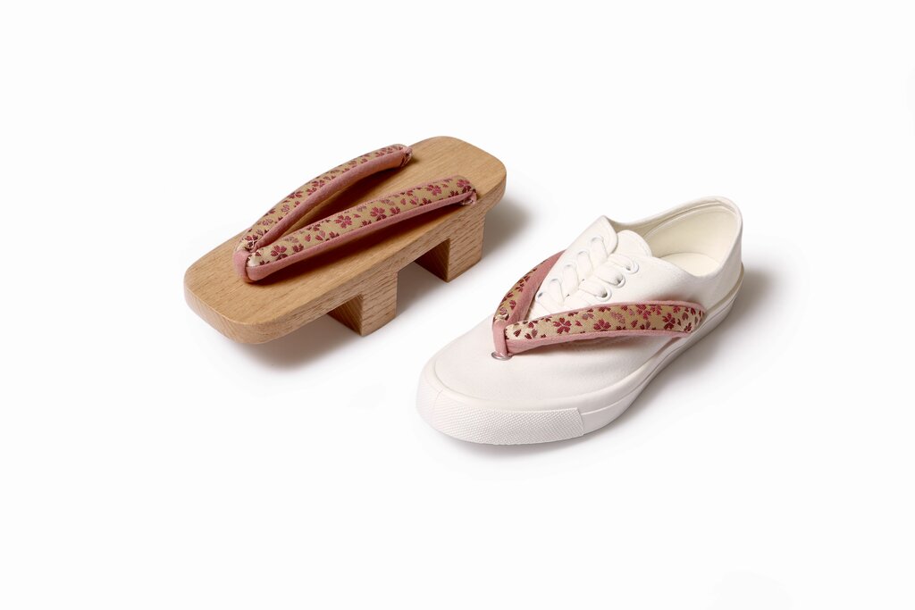 Ein weißer Sneaker neben traditionellen japanischen Geta-Holzsandalen auf weißem Hintergrund, ein Konzept, das moderne und traditionelle Schuhmode verbindet